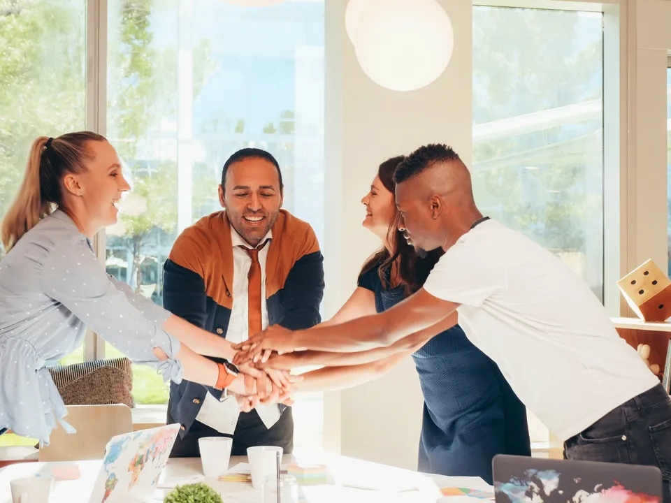 A team stacking hands together around a table in a sunny office